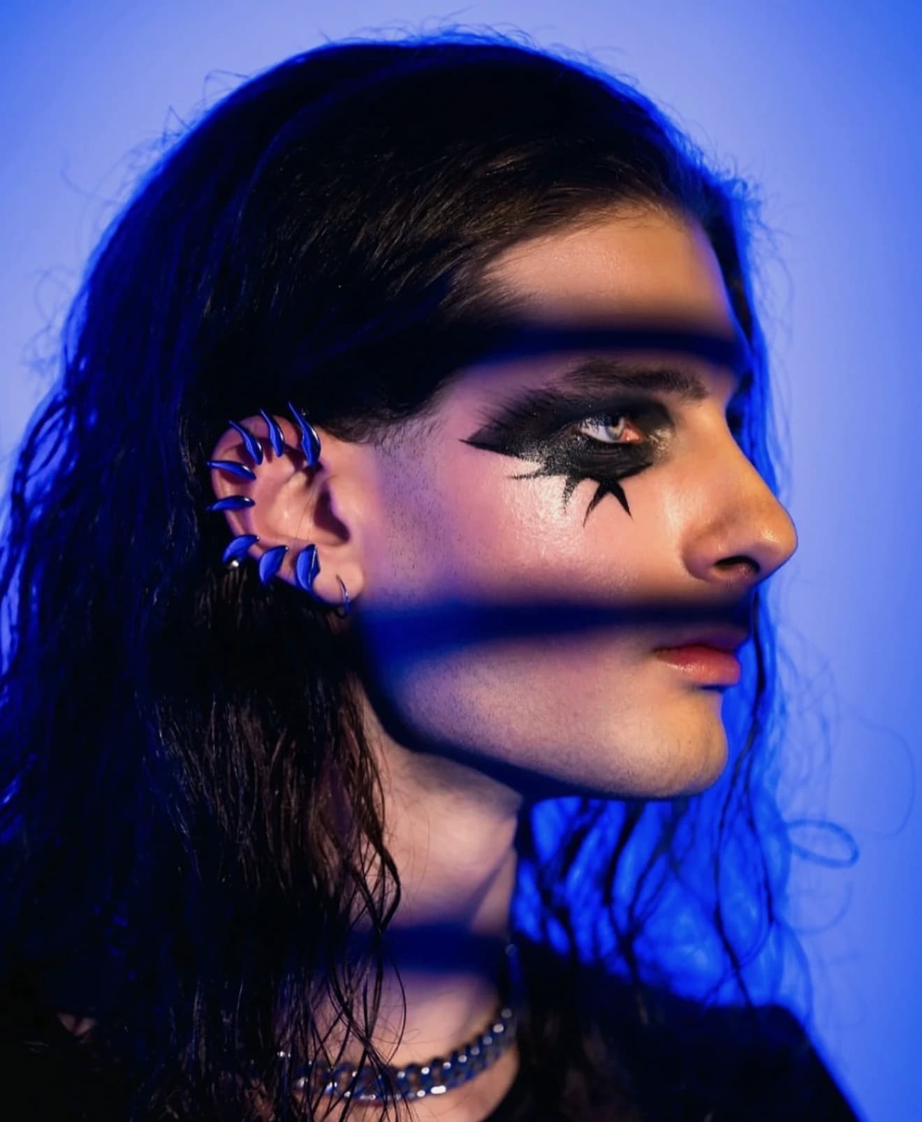 Creative black eye makeup photographed under vivid blue lighting.