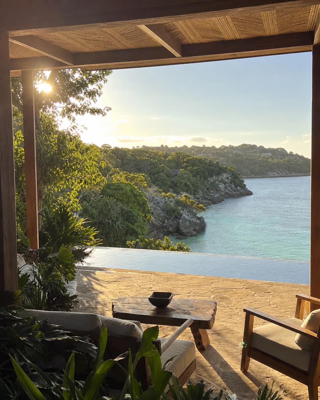 Sunlit resort terrace overlooking an infinity pool and quiet tropical cove.